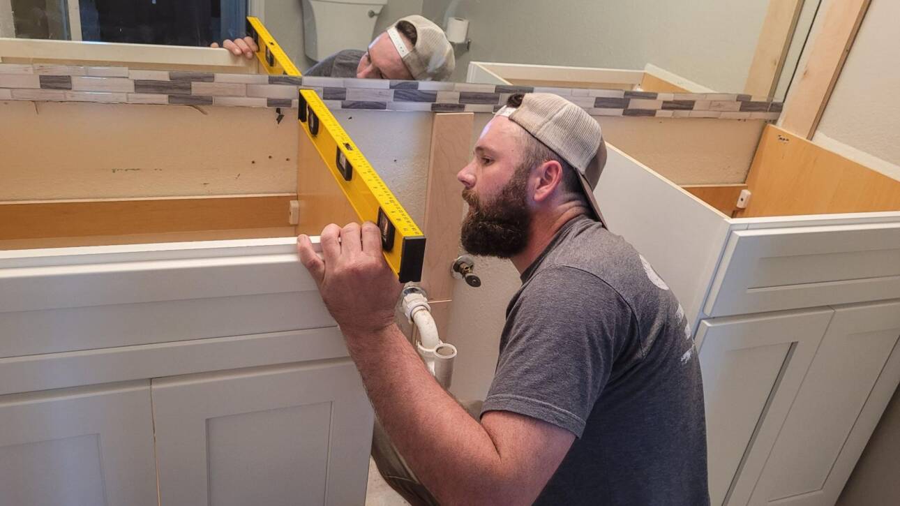 A cabinet maker checks the alignment and depth of a wooden kitchen cabinet with a level