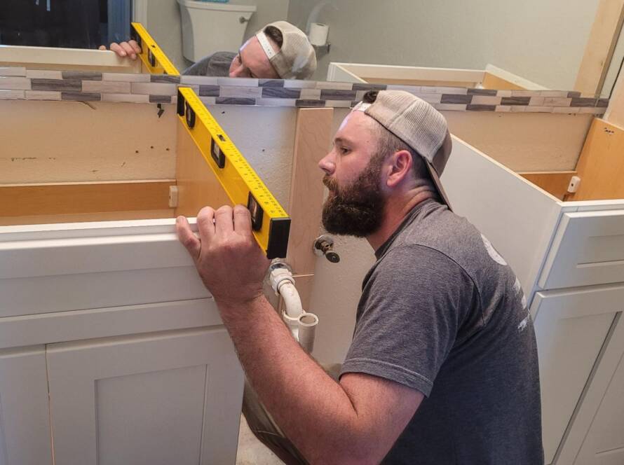A cabinet maker checks the alignment and depth of a wooden kitchen cabinet with a level