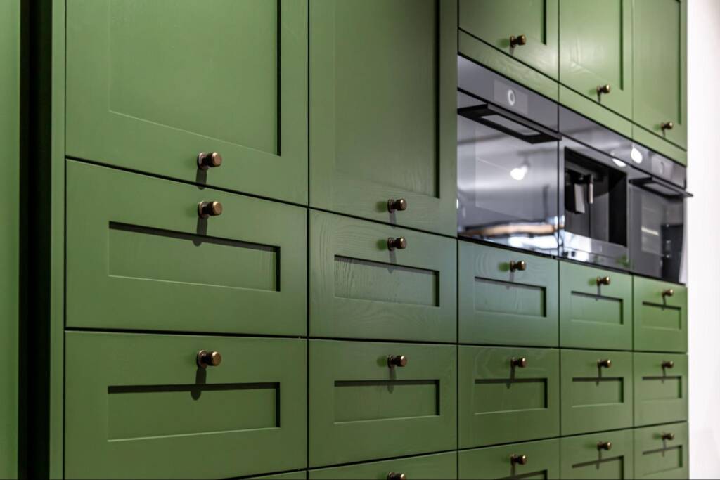Detailed view of green Shaker-style kitchen cabinets with chrome handles.