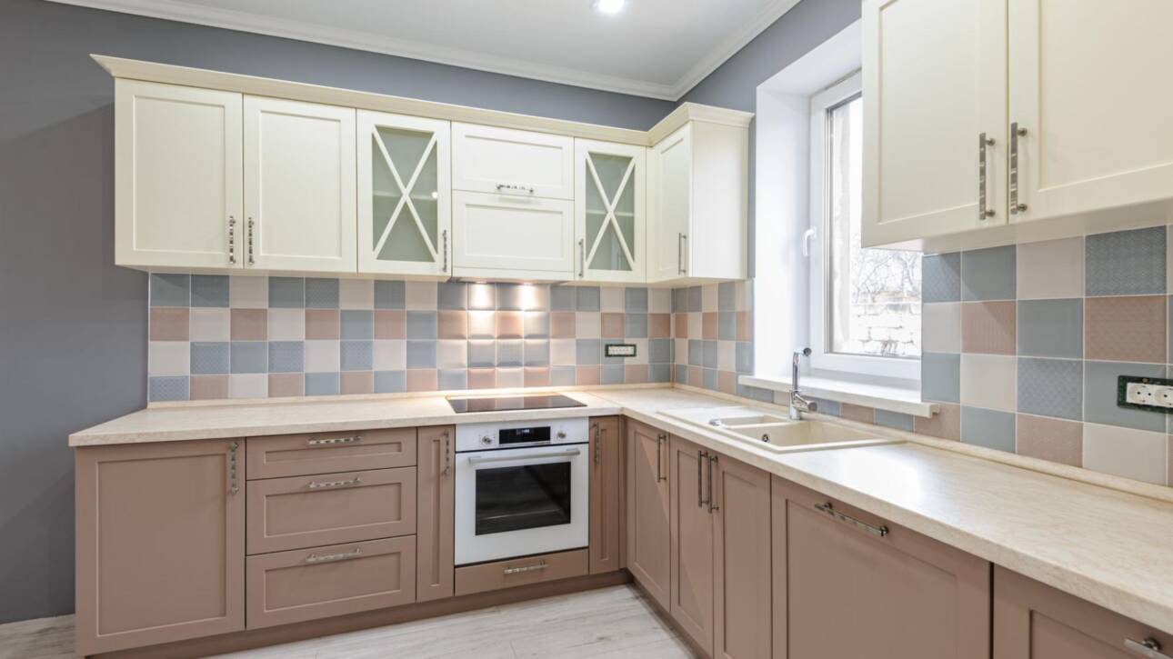 Luxury modern Provence-style kitchen with grey, pink, and cream cabinets and tiled backsplash.