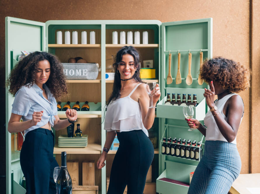 Three young women dance in a kitchen in front of a custom cabinet.