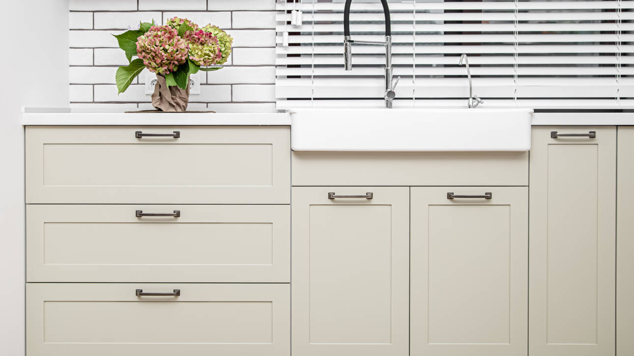 A kitchen sink outfitted with cream shaker cabinets for storage.