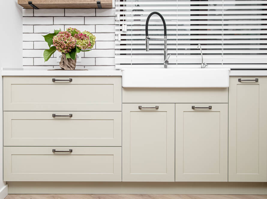 A kitchen sink outfitted with cream shaker cabinets for storage.